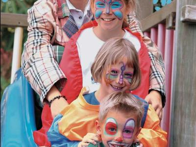 Trois enfants avec le visage peint et une femme souriante sur un toboggan extérieur.