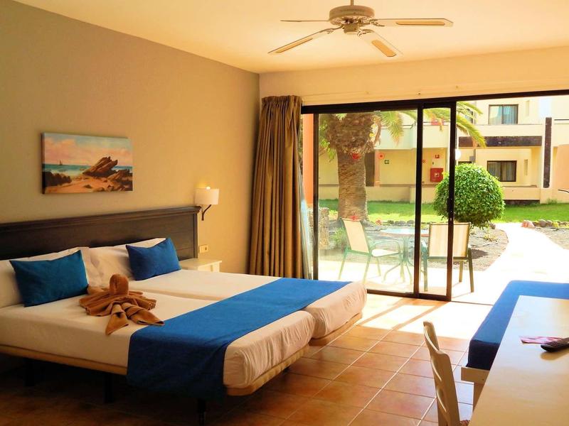 Chambre avec deux lits, accents bleus, télévision et accès à un jardin.