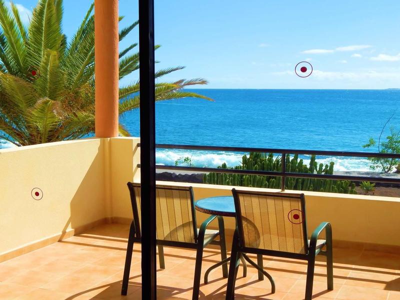 Balcon avec deux chaises et une table donnant sur la mer avec des palmiers en arrière-plan.