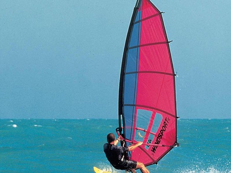 Une personne fait de la planche à voile sur une planche jaune avec une voile rouge sur la mer bleue.