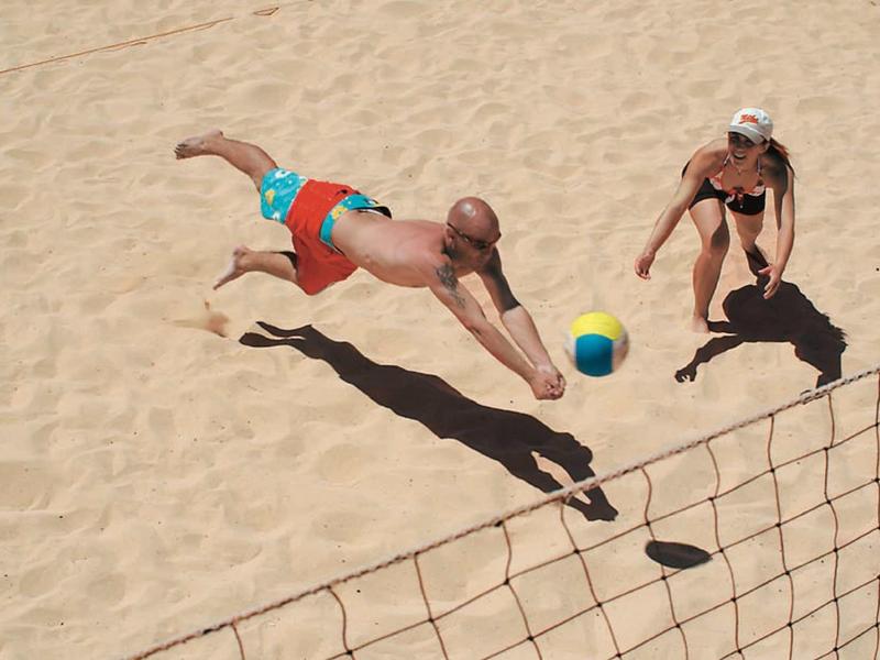 Deux personnes jouent au beach-volley, l’une plonge pour toucher le ballon.