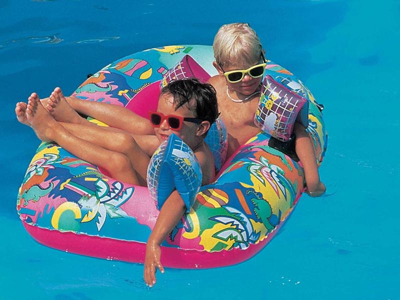 Trois enfants portant des lunettes de soleil sont assis dans une bouée colorée dans la piscine.