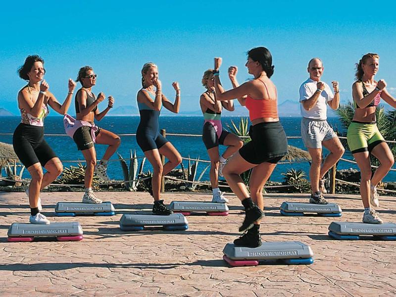 Groupe fait de l’aérobic avec step en plein air avec vue sur l’océan par temps ensoleillé.