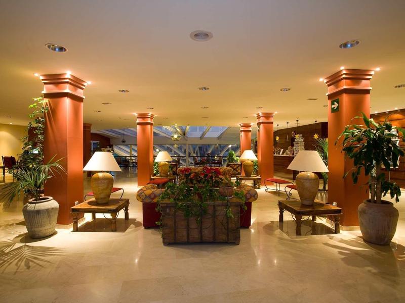 Hall d'hôtel avec colonnes, plantes et coins salon sous un éclairage chaud et accueillant.