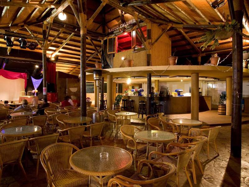 Restaurant chaleureux avec toit en bois et nombreuses tables avec chaises en rotin.