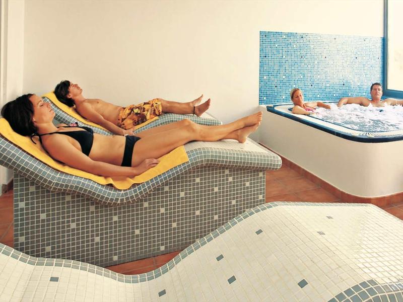 Trois personnes se détendent dans un espace bien-être avec bain à remous et chaises longues.