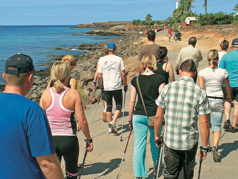 Groupe de personnes marchant avec des bâtons de randonnée le long d'une côte sous un ciel clair.