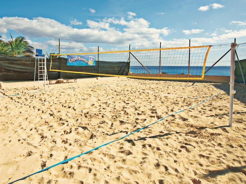 Terrain de volley-ball de sable extérieur avec filet et vue sur la mer sous un ciel clair.