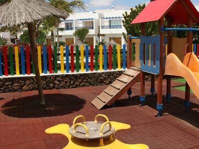 Aire de jeux colorée pour enfants avec toboggan et manège devant un bâtiment blanc