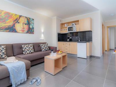 Helles Wohnzimmer mit brachem Sofa, Kissen, modernem Küchenbereich und buntem Wandbild.