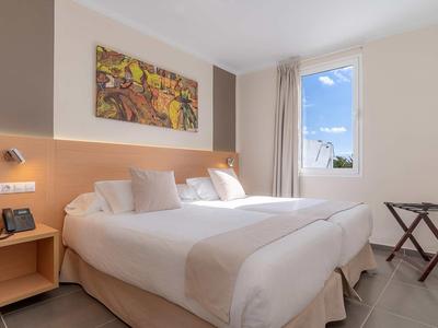 Helles Schlafzimmer mit großem Doppelbett, Holzmöbeln, Fenster und farbenfrohem Bild an der Wand.