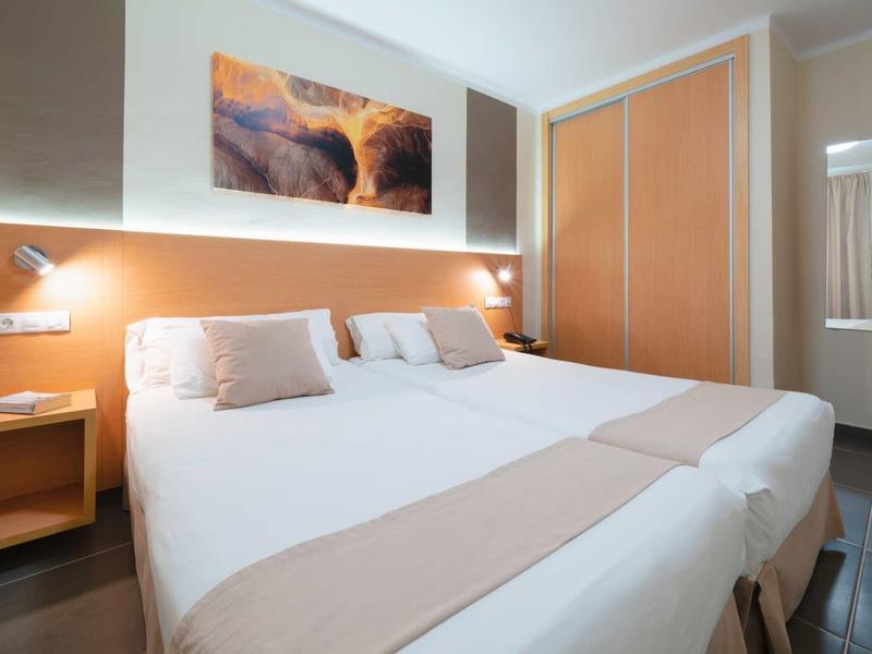 Modernes Schlafzimmer mit zwei Einzelbetten, Holzlattenrahmen, orangefarbenen Wänden und Landschaftsbild.