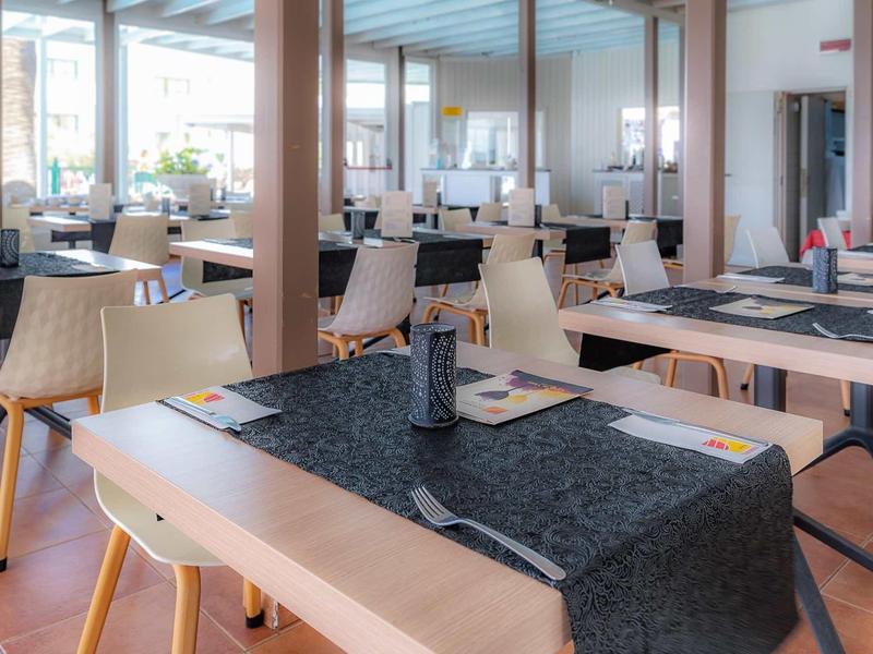 Hell eingerichteter Speisesaal mit Holztischen, schwarzen Läufern und beigen Stühlen.