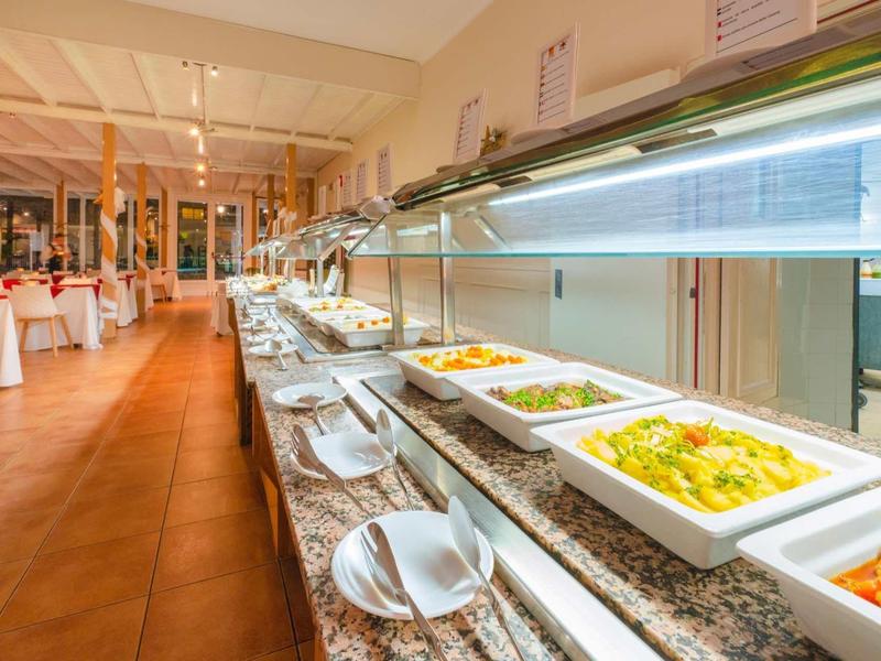 Buffet mit warmen Speisen in weißen Schalen auf einer langen Theke in einem hellen Restaurant.