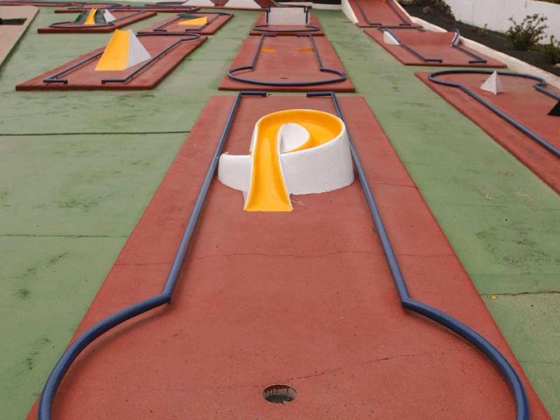 Minigolfbahn mit roten Spielflächen und blauen Begrenzungen unter bewölktem Himmel.