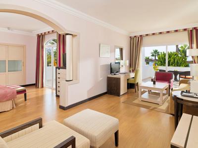 Helles Wohnzimmer mit Holzboden, bequemen Sesseln, großem Fenster und angrenzendem Schlafzimmer.