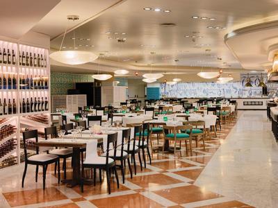 Großes modernes Restaurant mit weißen Wänden, Holzböden, Tischen, Stühlen und Weinregalen.