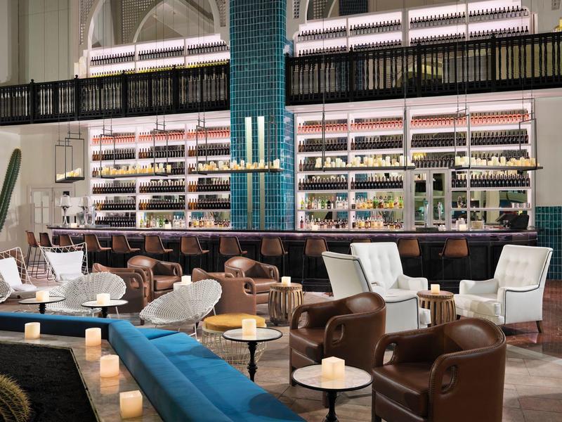 Bar elegante de hotel con sillones de cuero, sillas claras y estantería de vinos iluminada al fondo.