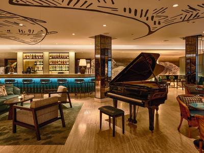 Espace lounge d'hôtel élégant avec piano, sièges et bar sous un éclairage chaleureux.