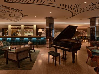 Bar elegante in hotel con pianoforte a coda, aree salotto e illuminazione soffusa.