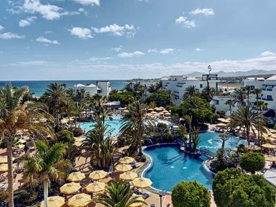 Hotelanlage mit Pool, Palmen und weißer Architektur unter blauem Himmel am Meer.