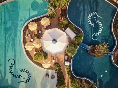 Vue aérienne d'une piscine avec une zone centrale et plusieurs parasols et chaises longues