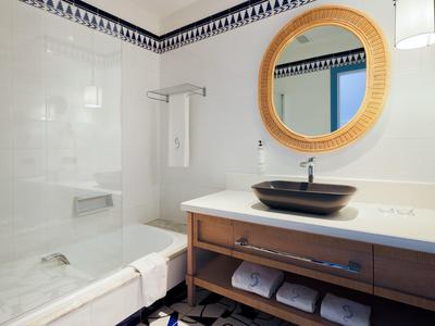 Bagno moderno con specchio rotondo, lavabo e vasca da bagno con parete in vetro.