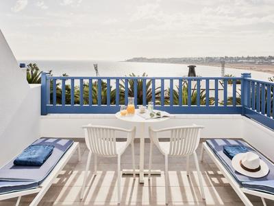 Terrazza con ringhiera blu, mobili bianchi e vista sul mare alla luce del giorno.