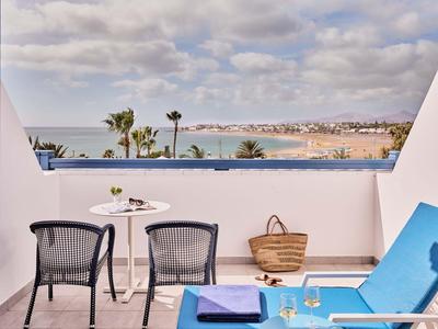 Balcon avec des chaises bleues et vue sur la mer sous un ciel partiellement nuageux