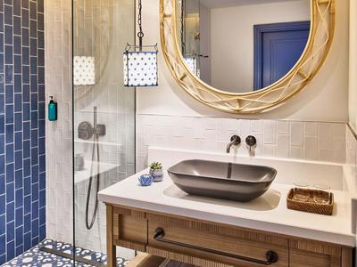 Salle de bains moderne avec miroir rond, lavabo gris et douche à effet pluie avec mur carrelé bleu.