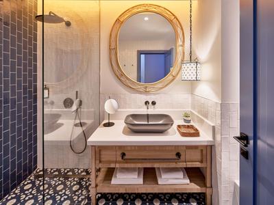 Salle de bain moderne avec miroir rond, lavabo gris et carrelage décoratif.