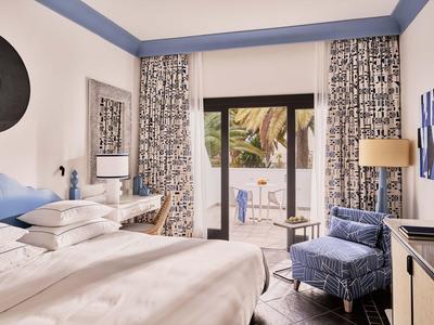 Chambre d'hôtel lumineuse avec lit double, accents bleus et balcon avec vue sur la mer.