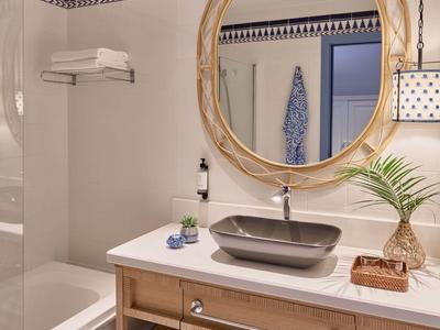 Salle de bain lumineuse avec miroir rond, lavabo gris et accents de carreaux bleus.