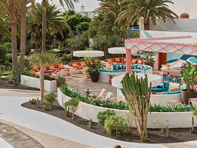 Espace extérieur d'un hôtel avec des tables, des chaises, des palmiers et une piscine au centre.