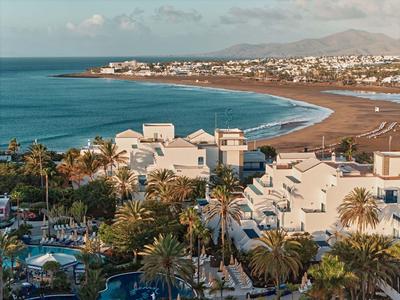 Vue d'une ville côtière avec plage, palmiers et bâtiments blancs sous un ciel bleu.