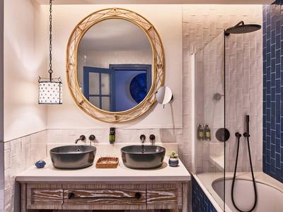 Salle de bain moderne avec doubles lavabos, miroir rond et baignoire avec accessoires noirs.