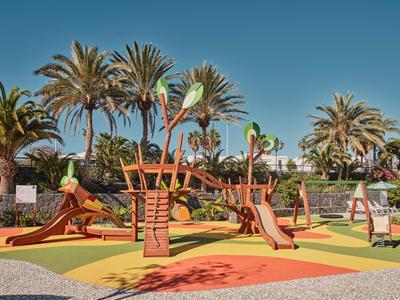 Aire de jeux pour enfants avec toboggans et équipements d'escalade dans une station hôtelière sous un ciel dégagé.
