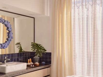 Chambre d'hôtel lumineuse avec un lit de traitement, un grand miroir et une fenêtre avec des rideaux.