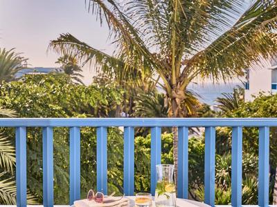 Balcon avec rambarde bleue, table et chaises blanches, décor tropical avec palmiers.