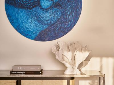 Salle moderne avec une œuvre murale circulaire bleue au-dessus d'une table en métal avec décorations et livres.