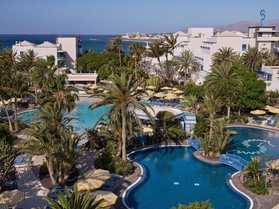 Hotel mit mehreren schwimmenden Pools und Palmen, Meer im Hintergrund unter blauem Himmel.