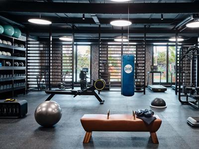 Moderne Fitnessraum mit Sportgeräten, Bänken und großen Fenstern mit Blick nach draußen.