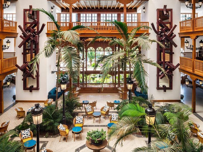 Ampio atrio dell'hotel con piante tropicali e architettura in legno classica.