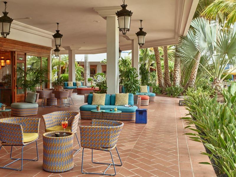 Terrazza coperta dell'hotel con aree salotto e vegetazione rigogliosa sul lato aperto.