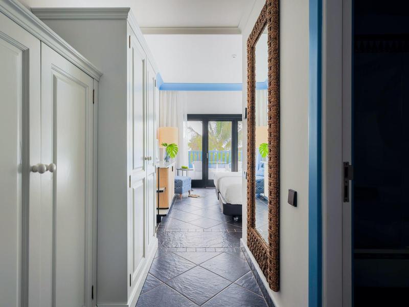 Vista di un corridoio con pareti bianche, pavimento piastrellato e grande specchio decorato sul muro.