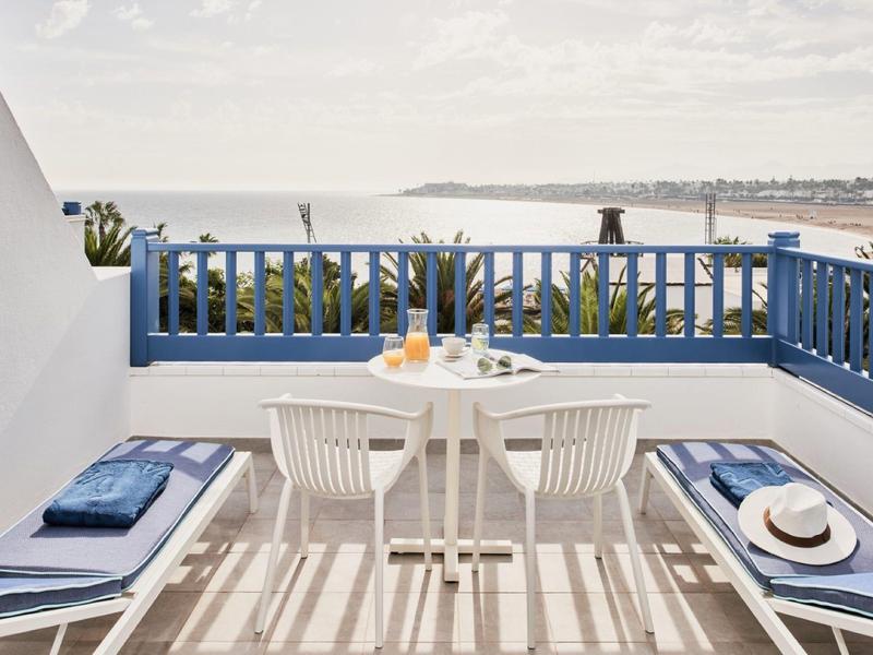 Terrazza con ringhiera blu, mobili bianchi e vista sul mare alla luce del giorno.