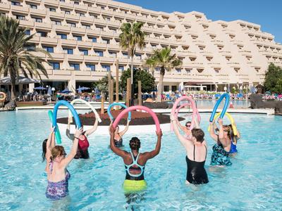 Several people are doing water aerobics in a hotel pool on a sunny day.