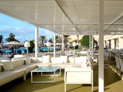 Terrazza dell'hotel con divani bianchi sotto un pergolato, vista piscina e palme.