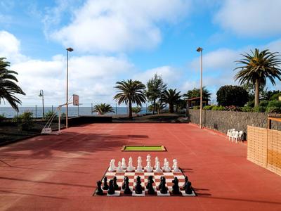 Outdoor chess game on red ground with palm trees and blue sky in the background.