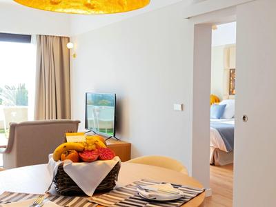 Moderner Wohnraum mit Obstkorb auf Tisch, Fernseher, Sessel und angrenzendem Schlafzimmer.